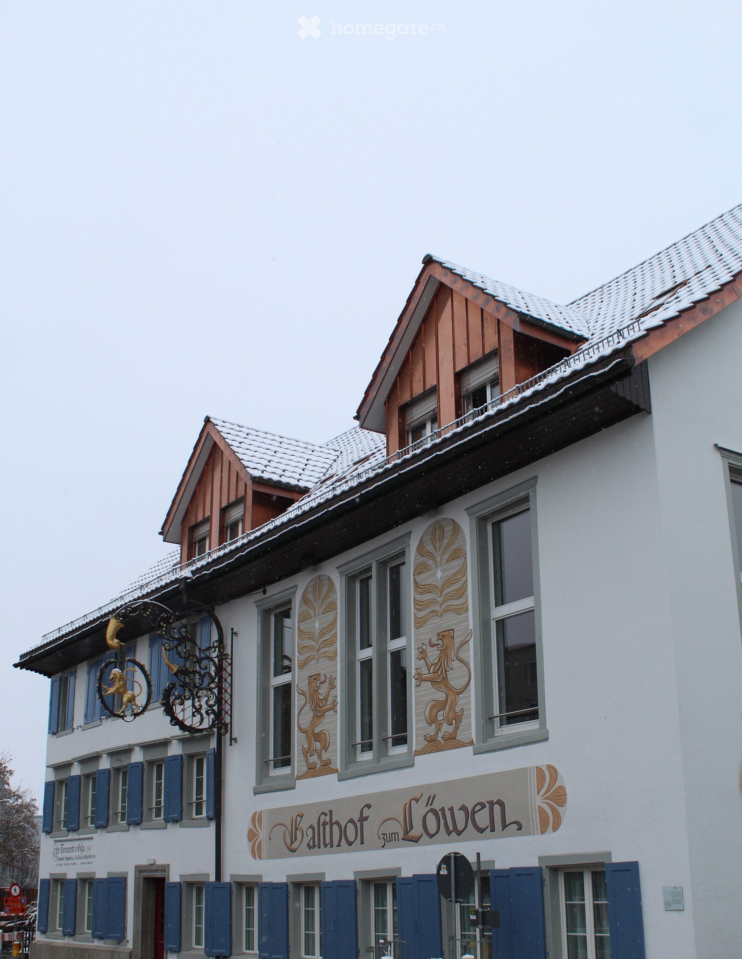 white house, blue shutters, logo and lion design on wall, snow on roof