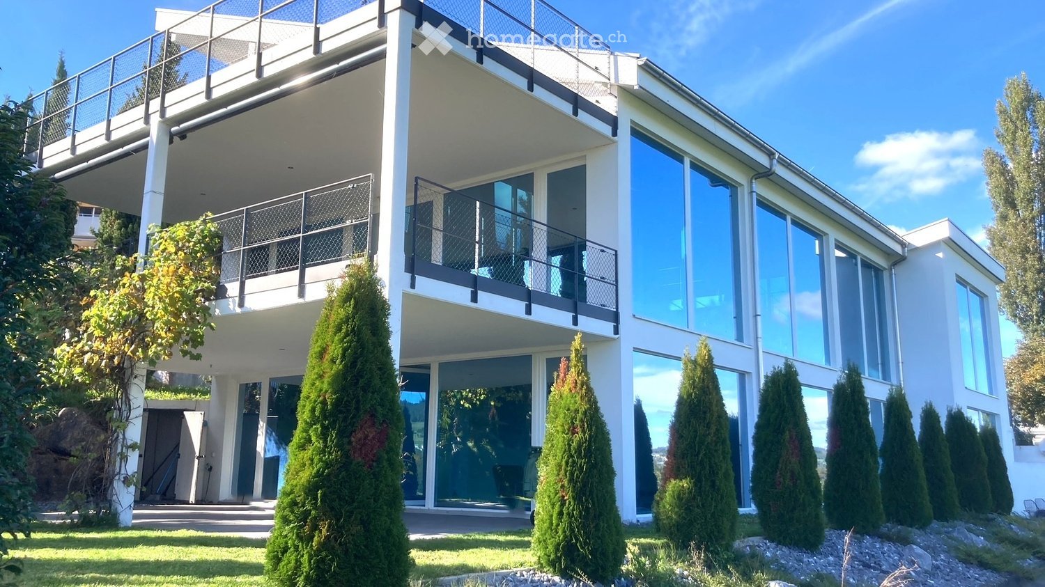 Modern house with glass walls, balcony, white exterior, two levels, large windows, green lawn