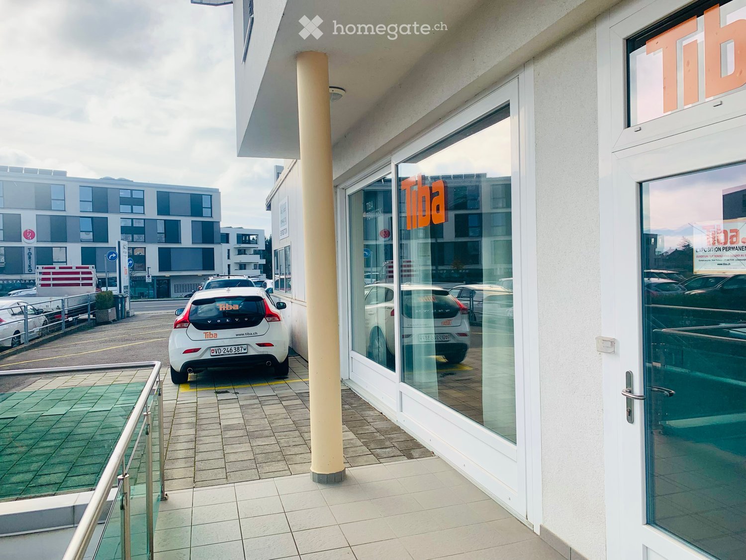 Entrance of building, parking space, multiple cars parked in the background