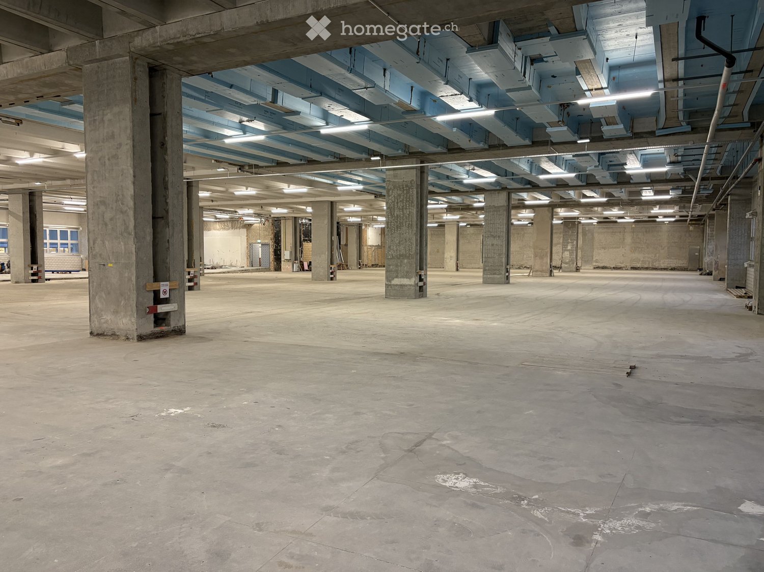 empty room with concrete pillars and blue beams, large open space, unfinished ceiling with exposed pipes and lighting