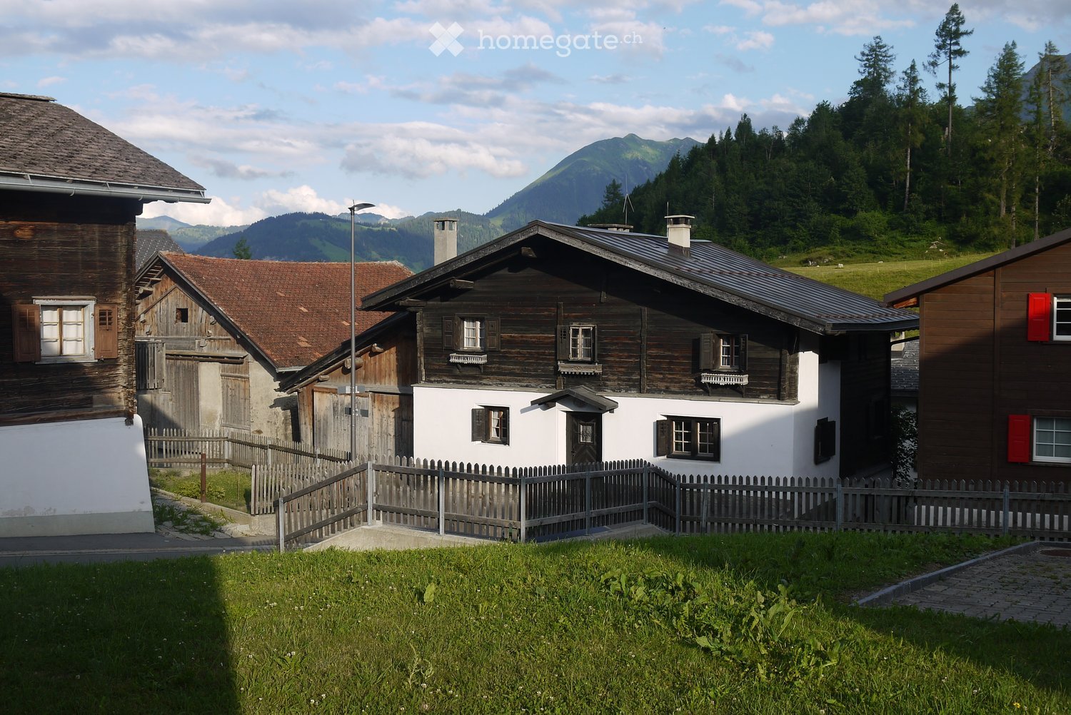 Traditional wooden houses with brown roofs and white walls, located in a mountainous area with a view of the mountains
