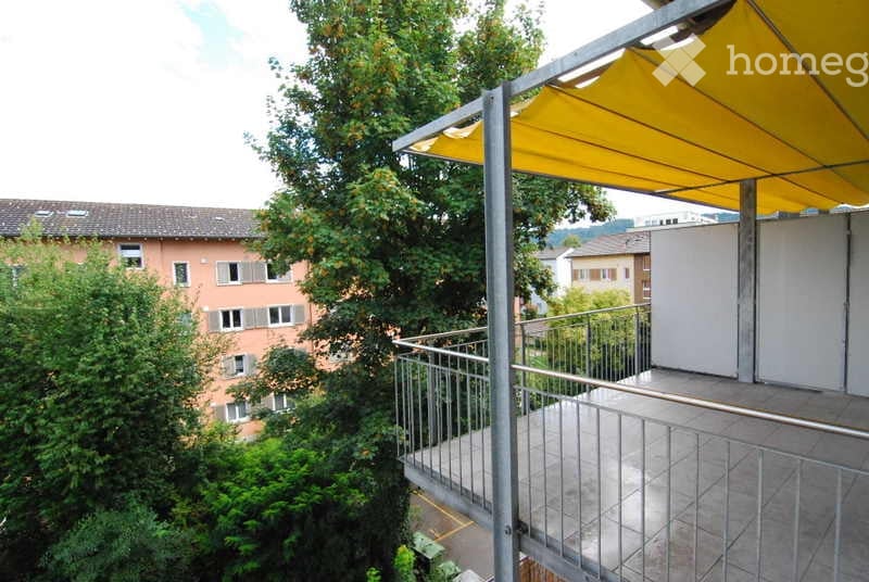 Balcony with metal railings and a retractable awning, surrounded by greenery.