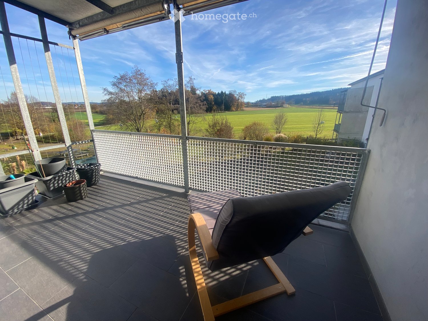 Balcony with metal railing, wooden lounge chair, metal grate, outdoor pots, floor view