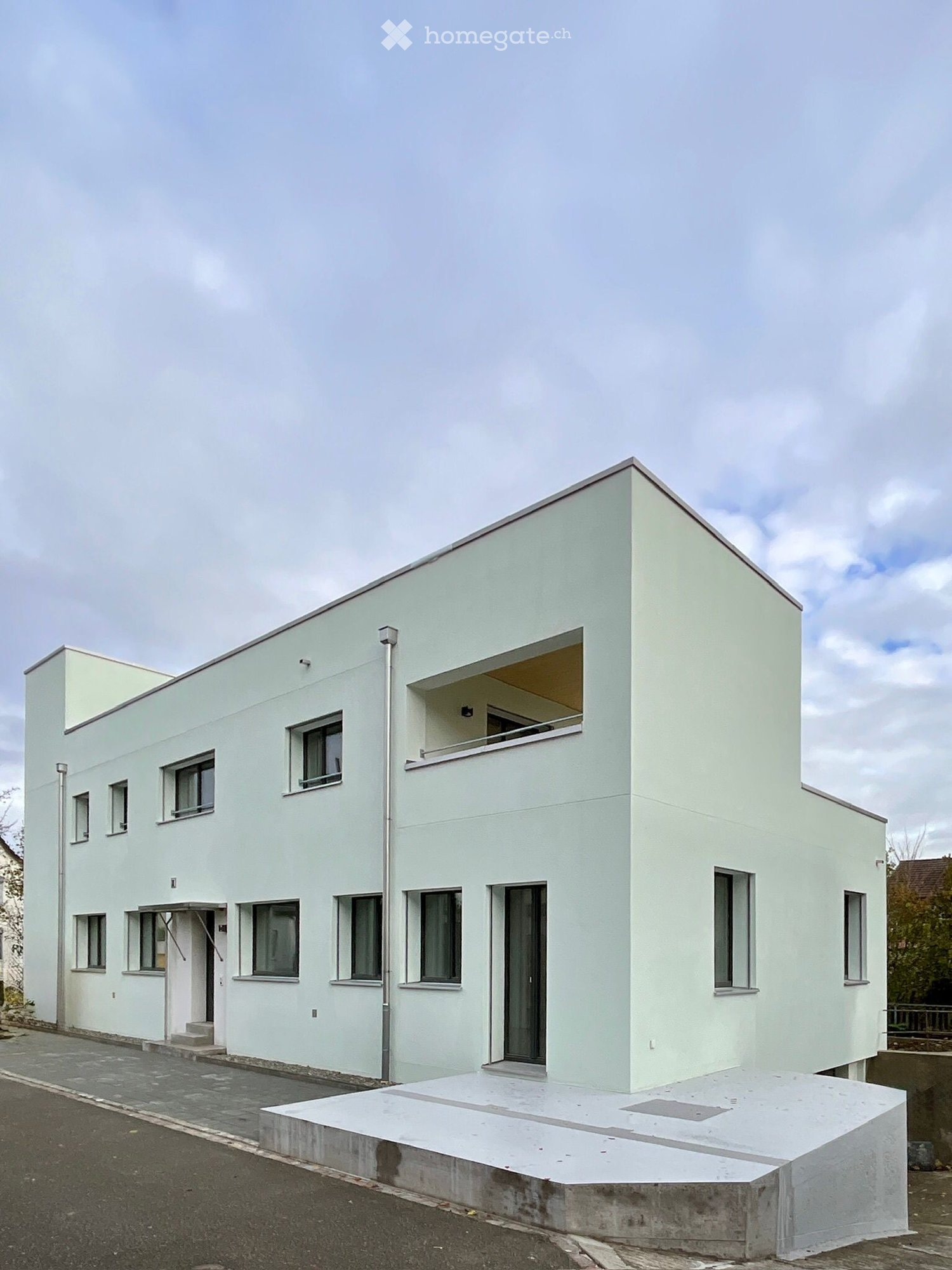 Two-story house, white exterior, multiple windows, front entrance, raised ground floor, potential balcony at the second floor