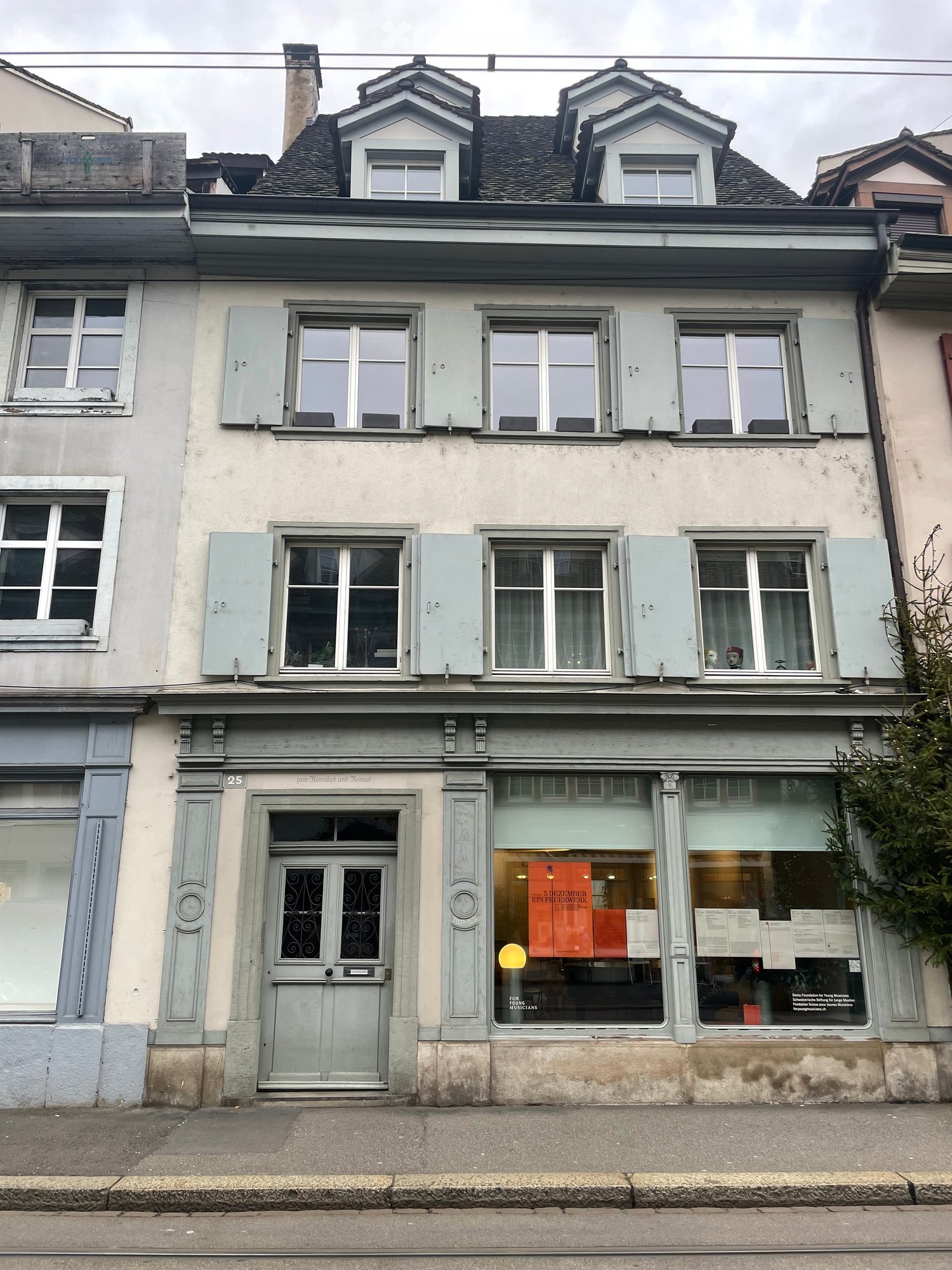 4 story building with several windows and a central entrance door. One window has a visible advertisement poster inside.