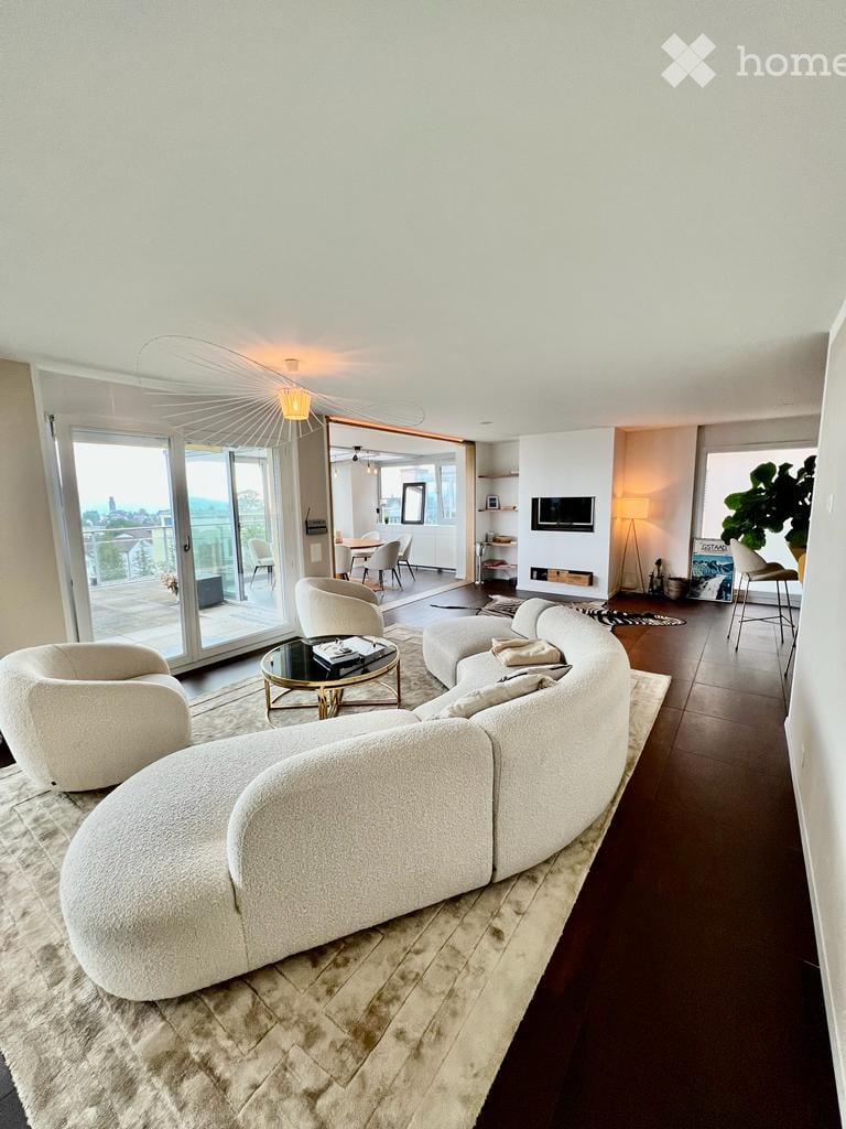 large curved white sofa, rug, coffee table, sliding glass doors to balcony, dining area, TV, lamps, plants