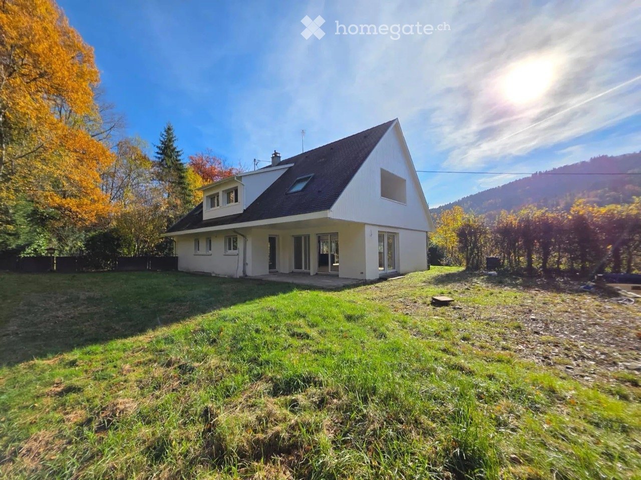 Single story house, white exterior, black roof, glass doors, surrounded by trees and grass