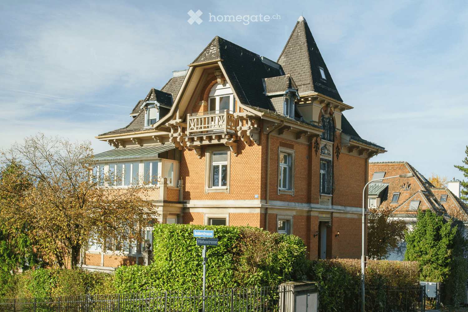 Extensive brickwork, pitched roof, numerous arched windows, ornate balcony with railing, multiple levels