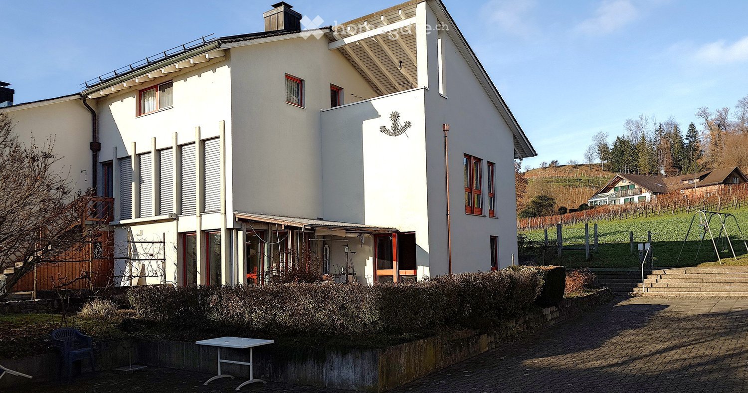 two story house, white exterior, red window frames, brick paved driveway, garden with shrubs