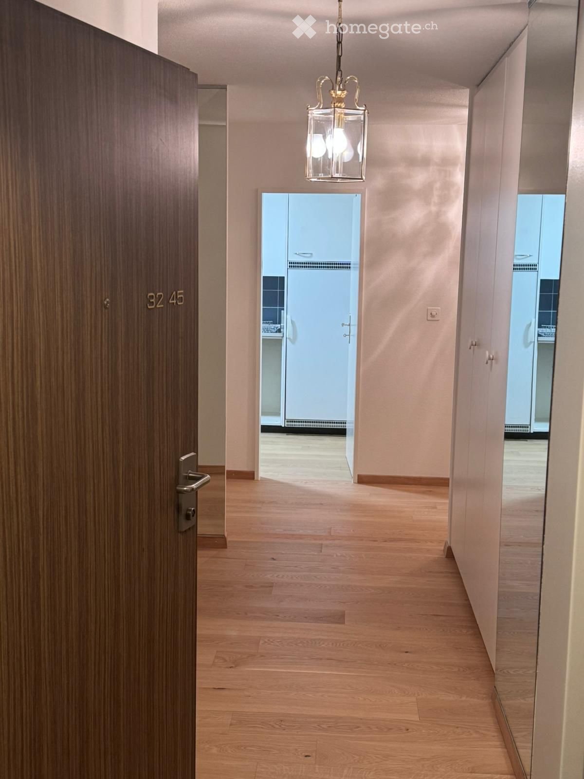 Wooden door, wooden floors, white walls, pendant light, open door to another room with white cabinetry and tiled wall, mirrored wardrobes