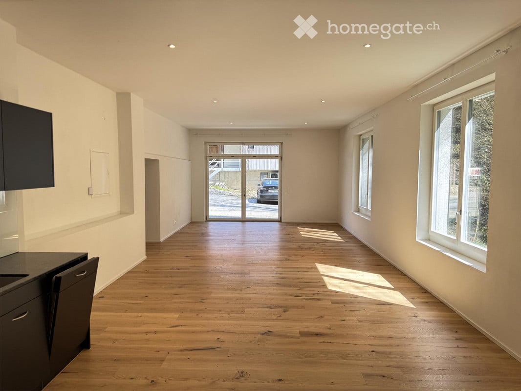Empty room with white walls and wooden floor, sliding doors leading to a garage, two windows