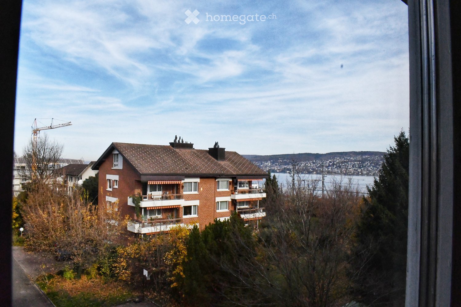 Exterior view of a multi-story brick building with balconies, surrounded by trees and a clear view of the lake.