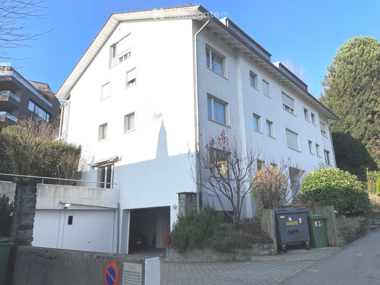 3-storey building, white exterior, multiple windows, attached garage, ground-level parking, trees, shrubs