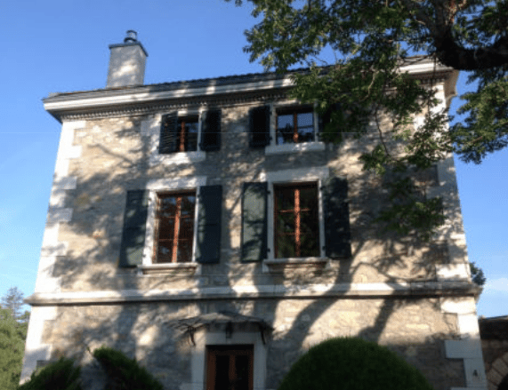stone house, multiple windows, chimney, wooden door, awning, trees, shrubs
