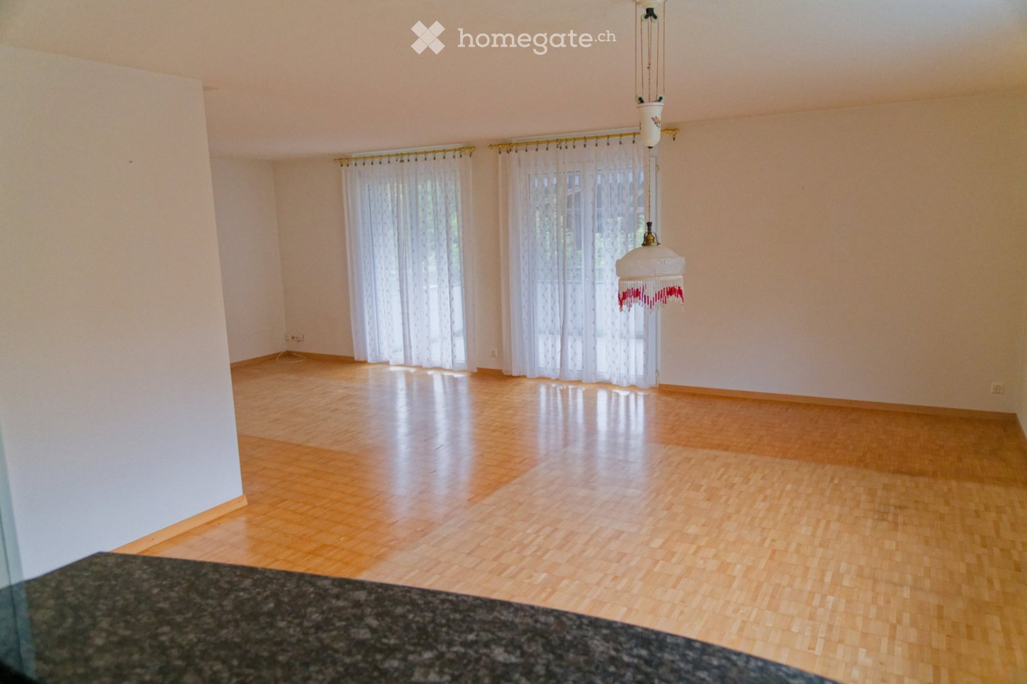 empty room with white walls, wooden floors, large white curtains, hanging light
