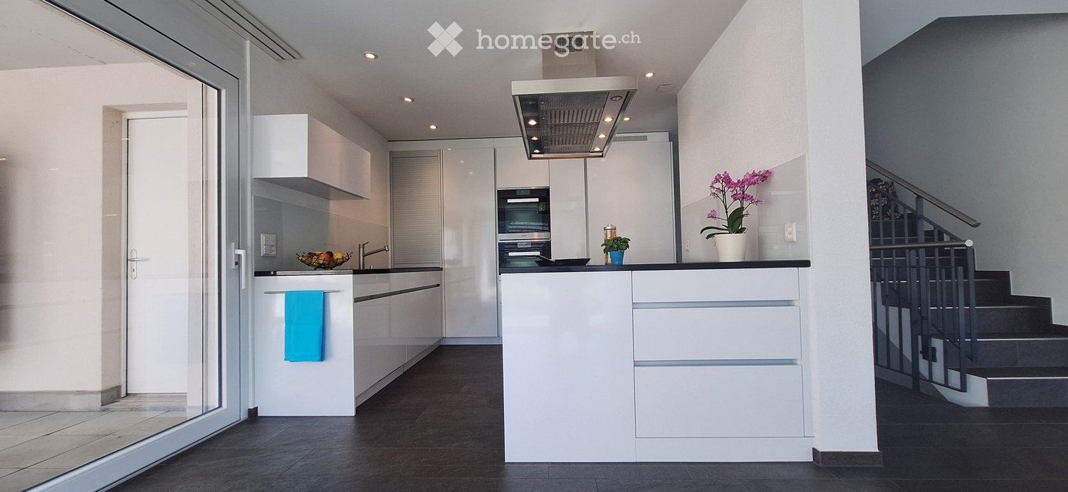 Modern, open-concept kitchen with white cabinets, black countertops, stainless steel appliances including a dishwasher, and a large window providing natural light.
