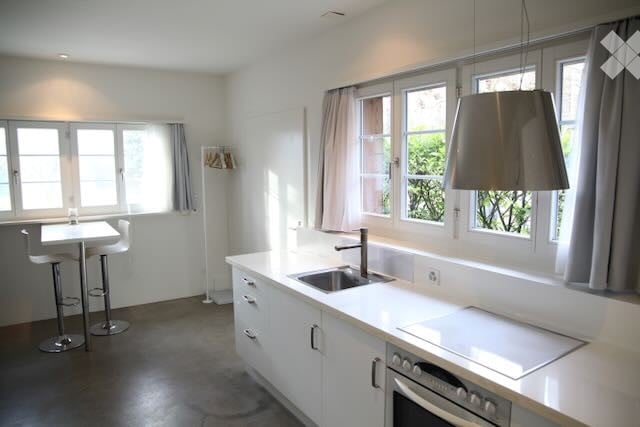 Modern kitchen with white cabinets, dark concrete floor, large windows, built-in appliances, and an island with stools.