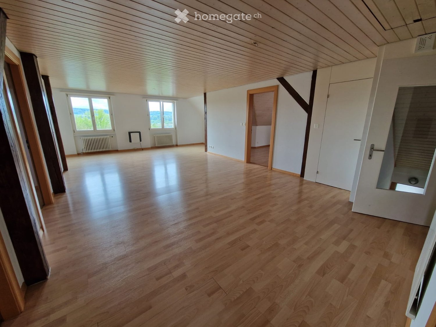 large empty room with wooden floors, two windows, white walls, white ceiling, heaters, open door