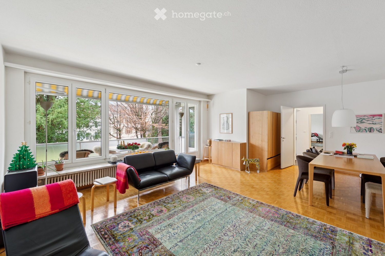 modern furniture, wooden floor, large windows with balcony, couch, dining table with chairs, area rug, side table, cabinets, decorative items, and Christmas tree