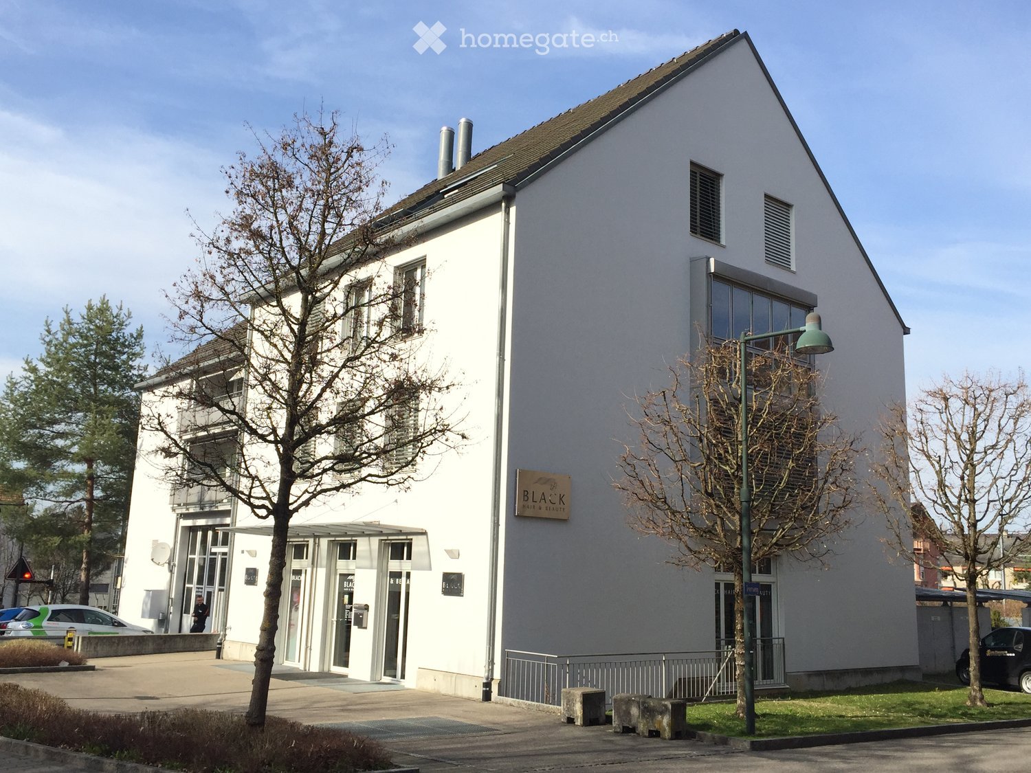 White building with 3 stories, 2 chimneys, glass windows, entrance, signboard with the text 'BLA&K' on the right side