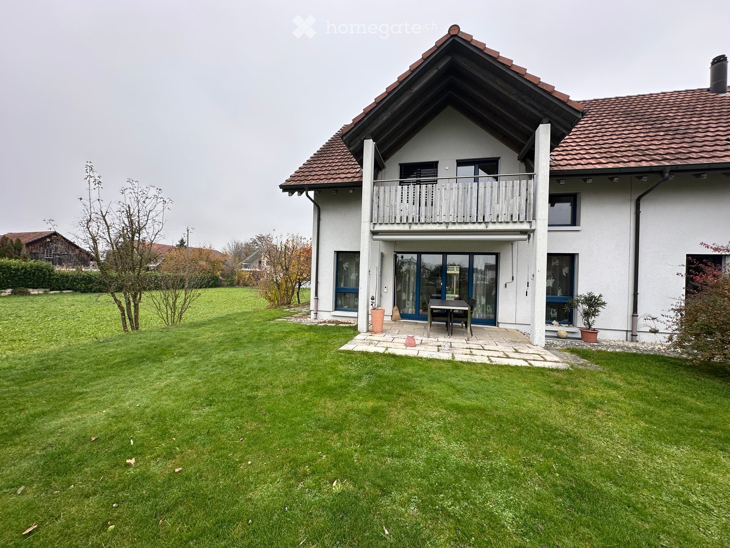 modern 2-story house, white exterior, brown roof, large balcony, paved patio, lush green lawn, outdoor table and chairs, potted plants