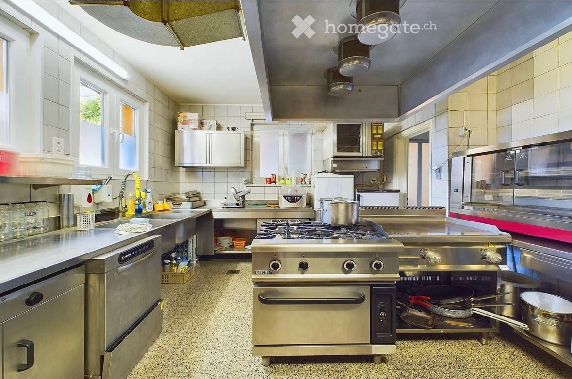 industrial kitchen, stainless steel countertops, oven, stove, sink, cabinets, tiled walls, windows, ceiling lamps