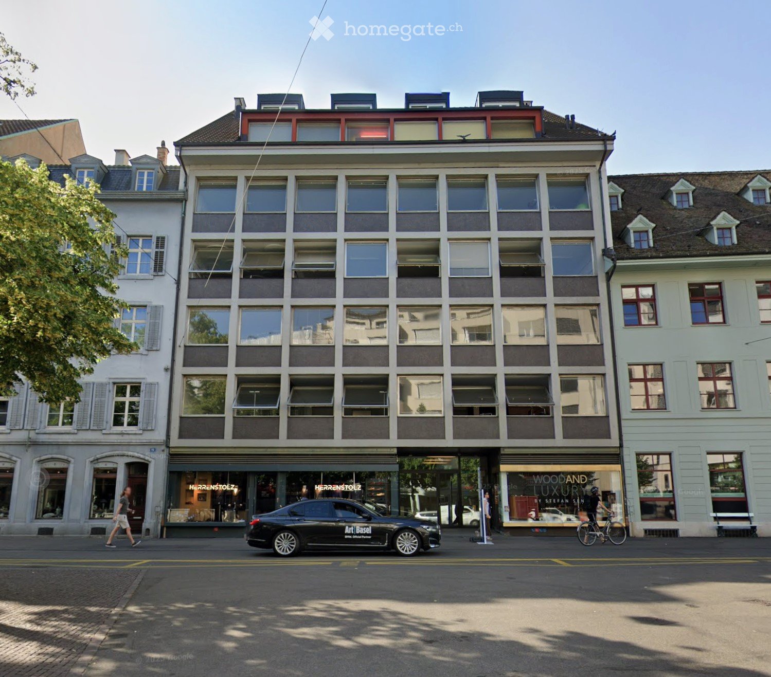 A modern commercial building with several floors, large glass windows, a tiled roof, and a car in front.