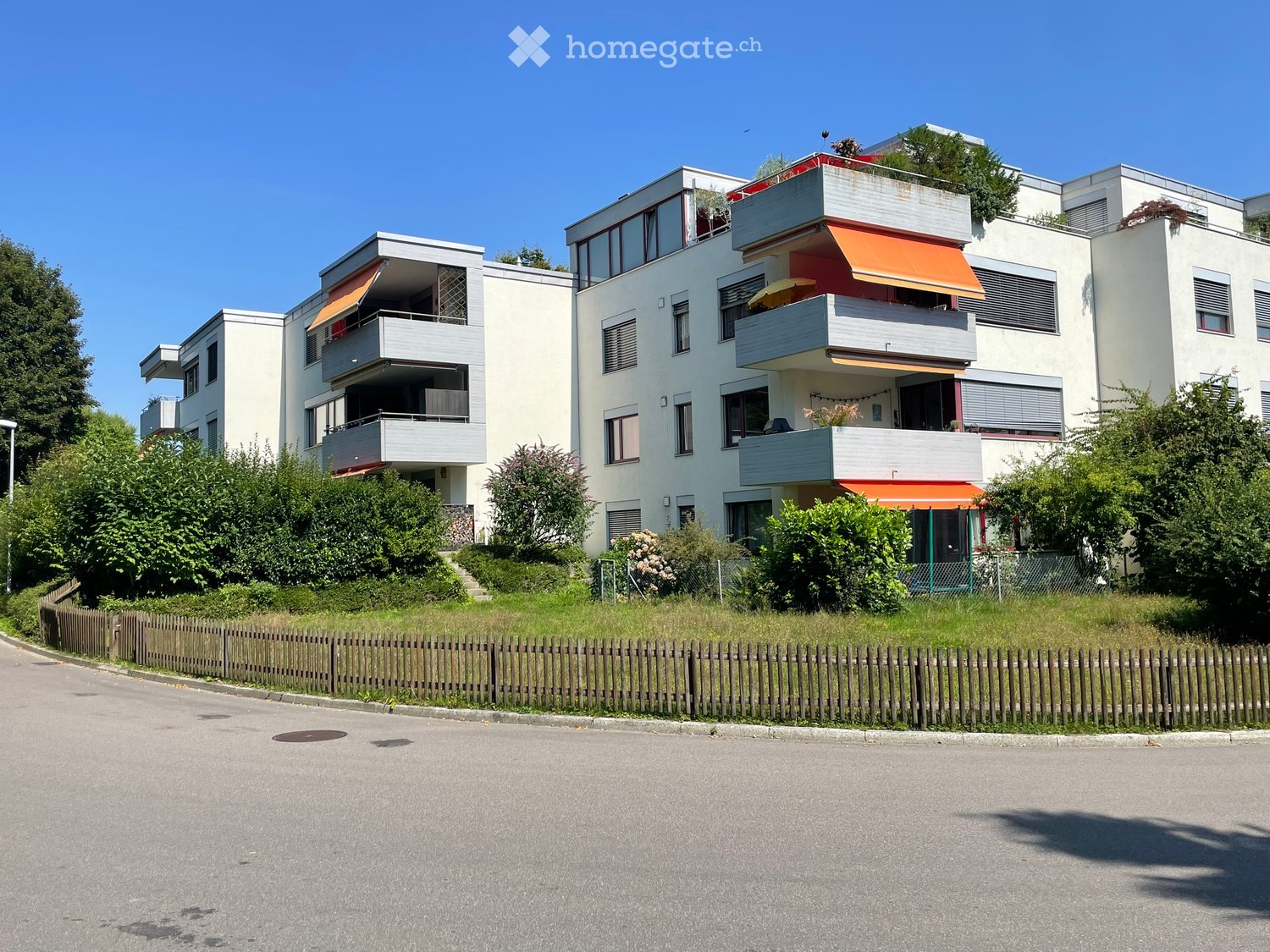 Three story apartment building, balconies, fenced yard, trees