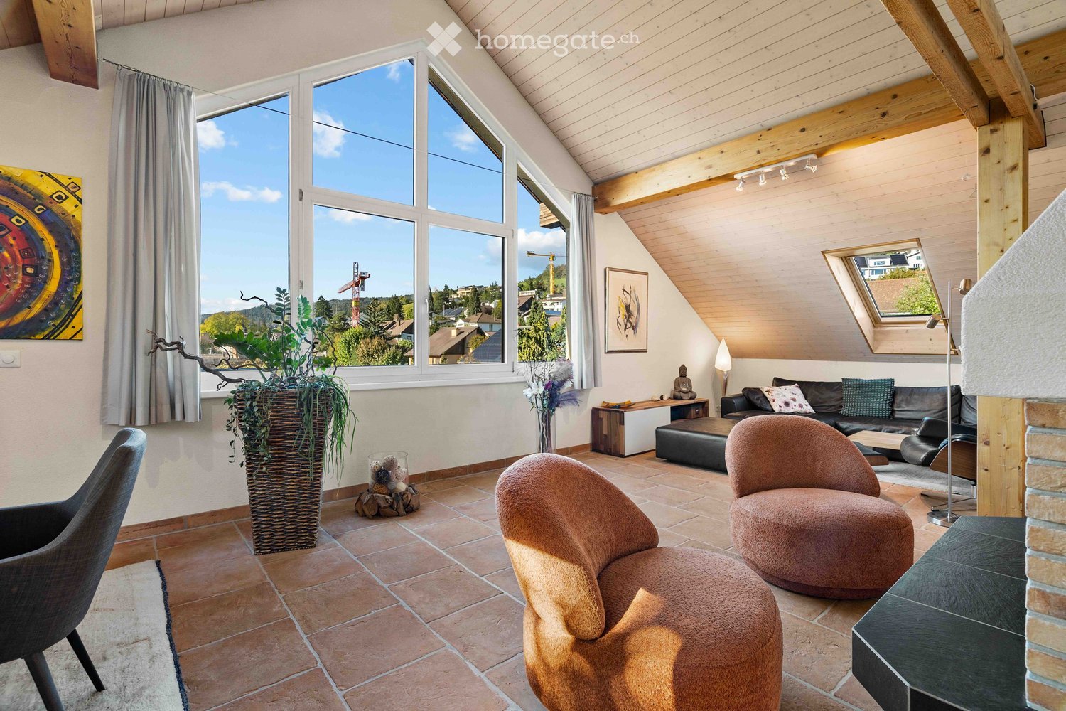 Large window, fireplace, wooden ceiling, two couches, two armchairs, floor lamp, artwork, rug