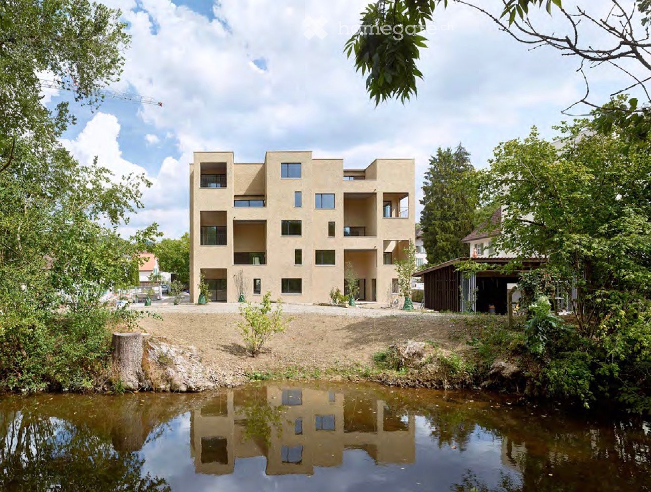 modern multi-story apartment building, beige facade, surrounded by trees, located near water