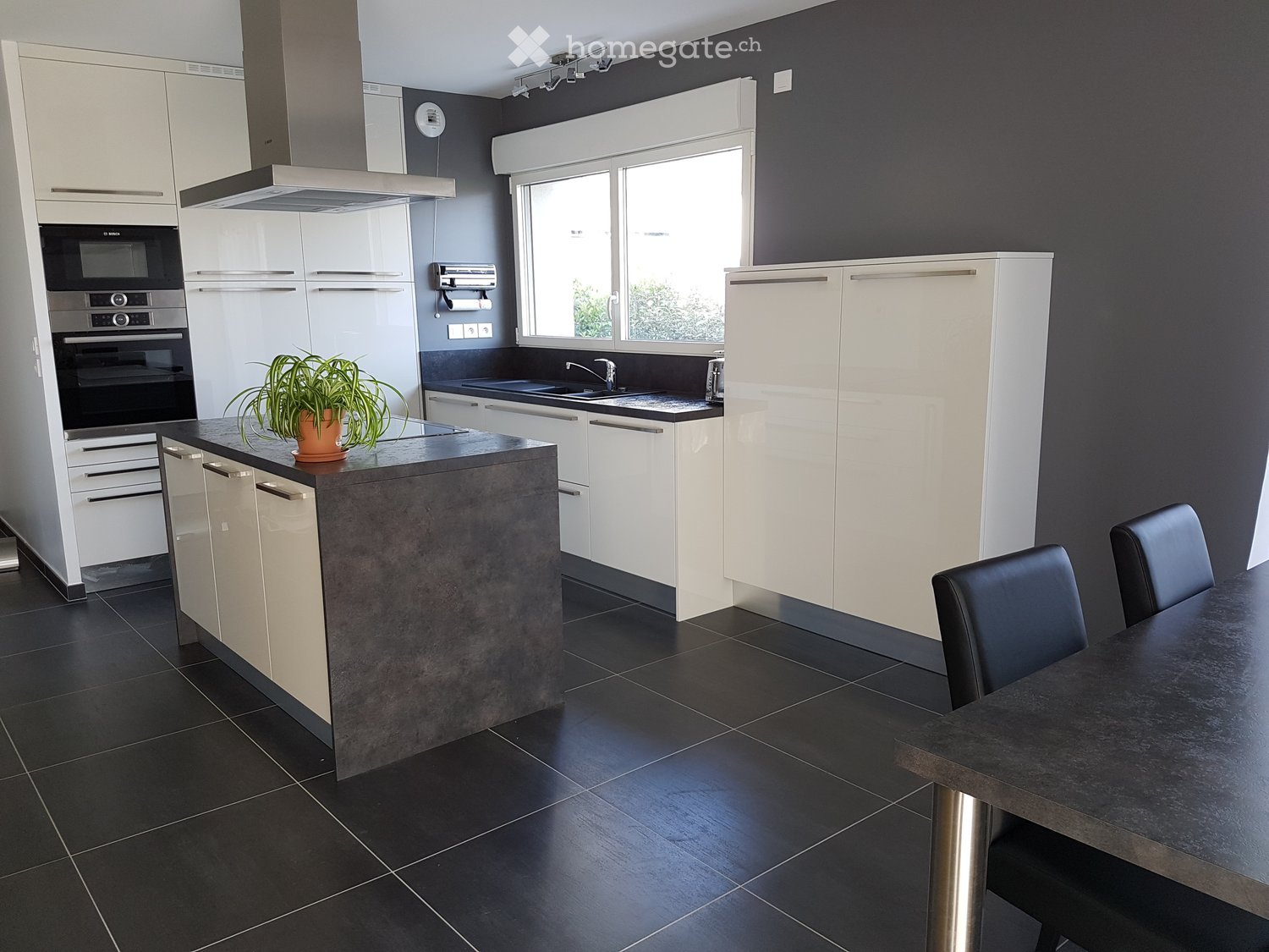 Modern kitchen with gray walls, black tiles, white cabinets, island with granite countertop, oven and microwave, sink with faucet, dining table with chairs