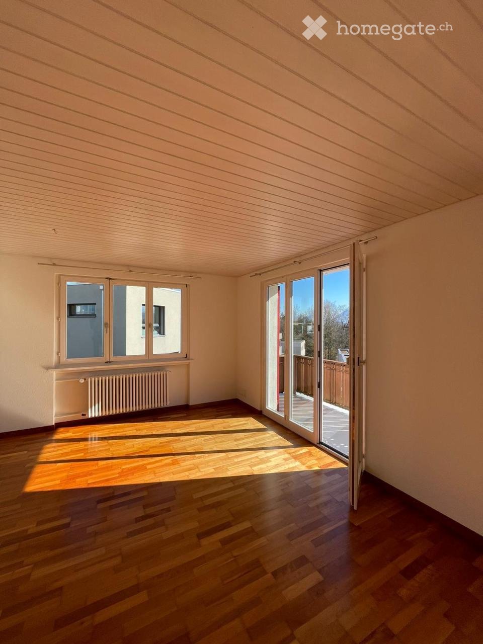 large room, sliding glass doors leading to balcony, windows, white walls, wooden floors, heater