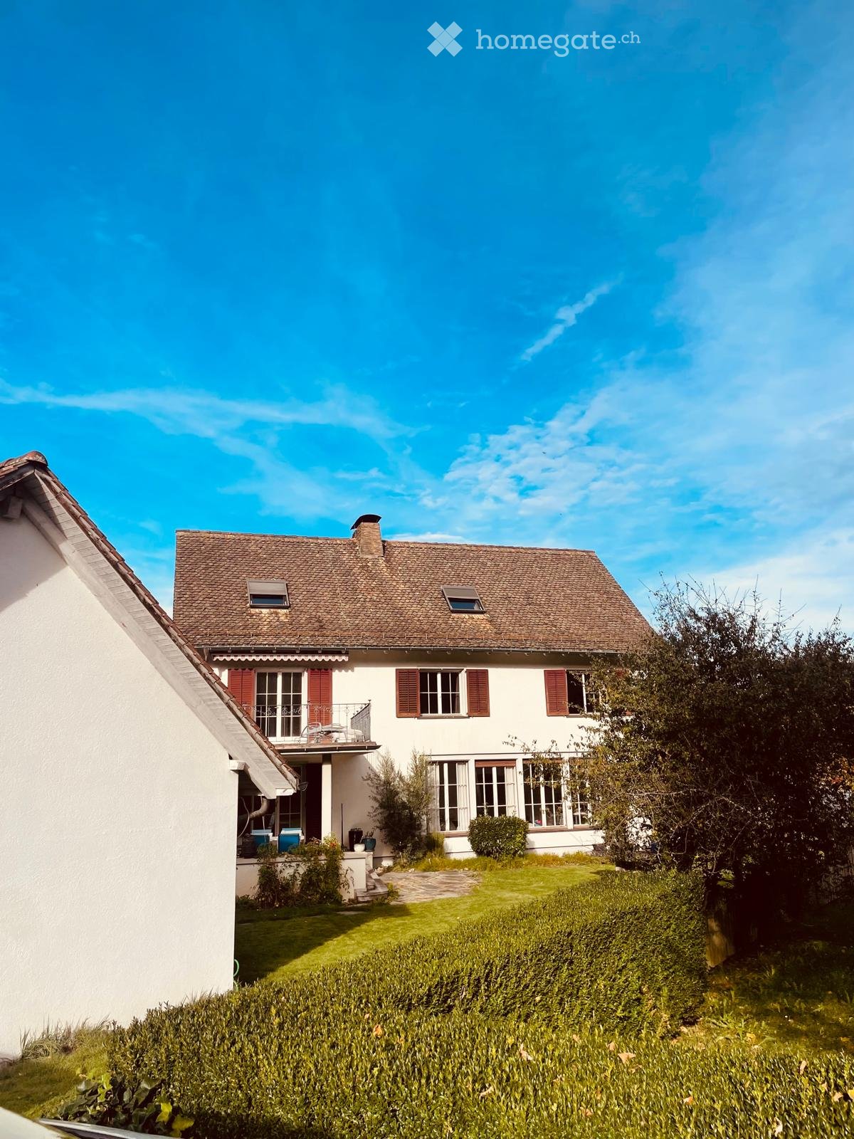 2-story house with a brown roof, red shutters, large windows, terrace, garden, shrub, and plants
