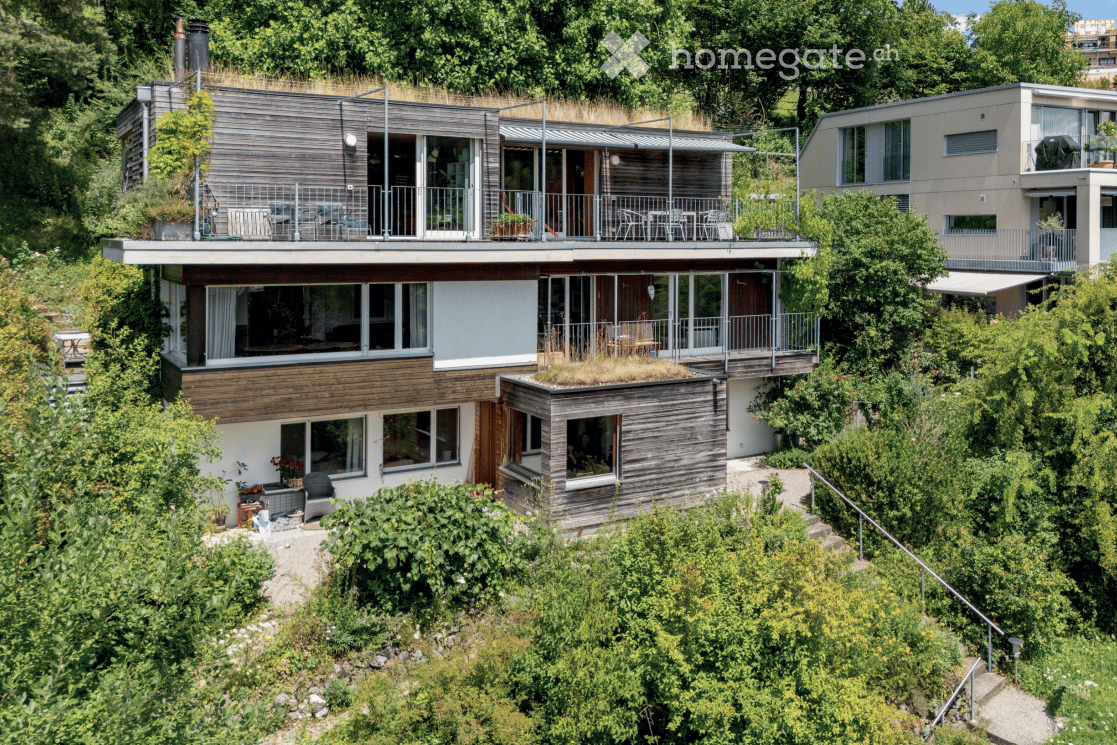 Two-story house with roof terrace, balconies, wooden facade, nestled among trees
