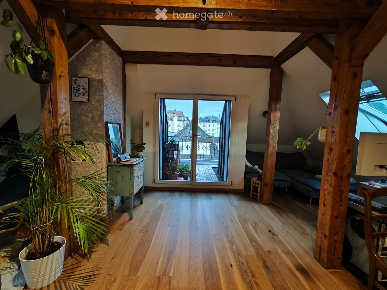 attic, hardwood floors, wooden pillars, sliding doors to balcony, framed picture on wall, mirror, plants, sofa, desk, window