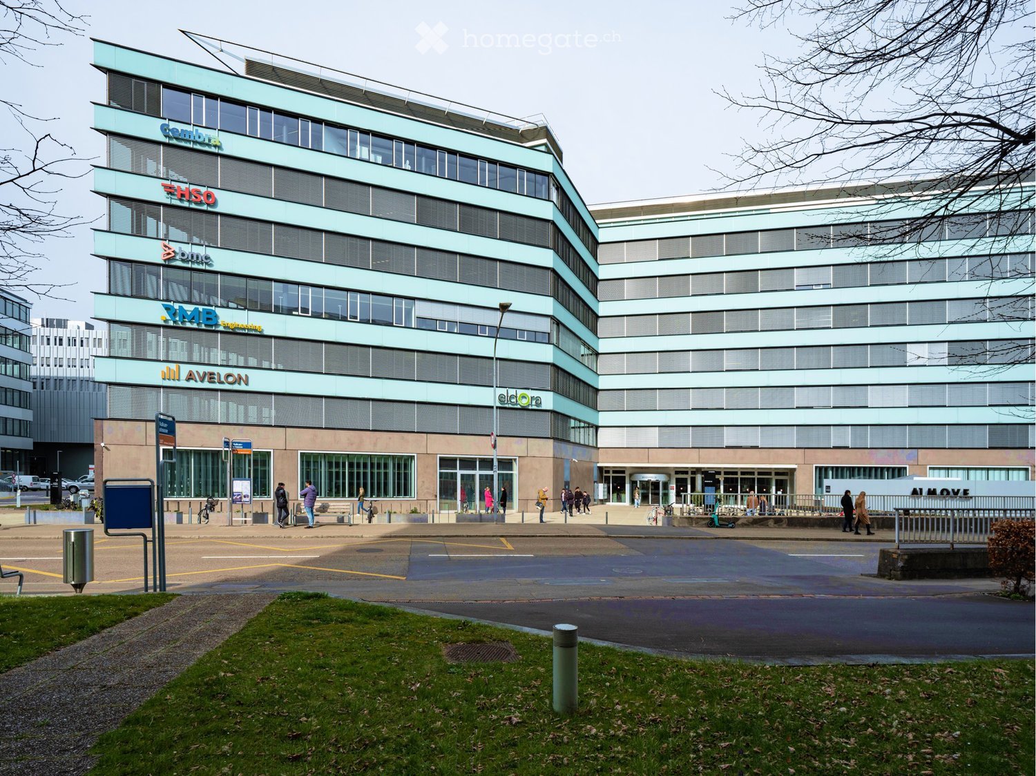 multi-story office building, large windows, front entrance, street-level shops, parking area
