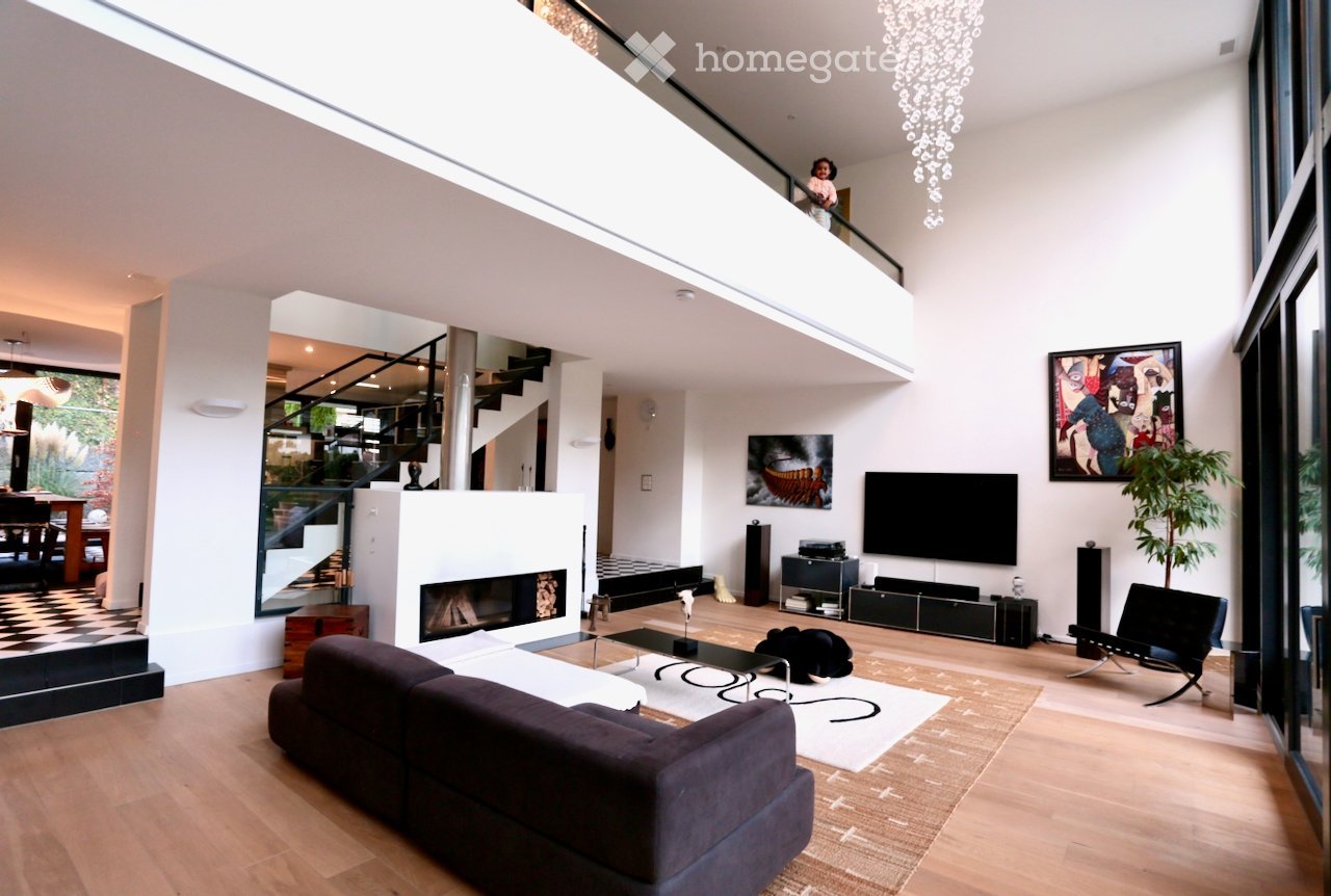 Open-plan living area, fireplace, white walls, wooden flooring, modern decor, chandelier, sofa, coffee table, entertainment center, flat screen TV