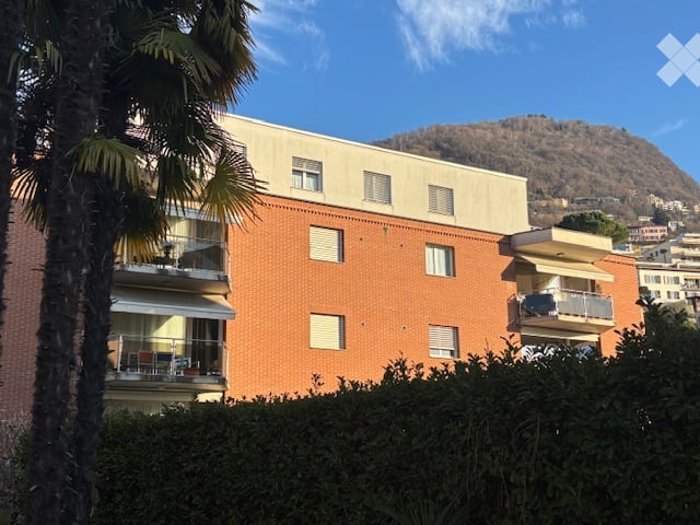 Modern apartment building, multiple balconies, fenced yard, mountain in the distance