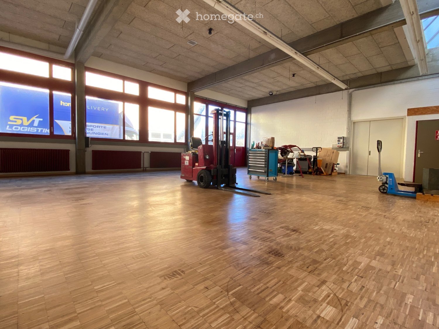 spacious room with large windows, warehouse equipment present, hard wooden flooring