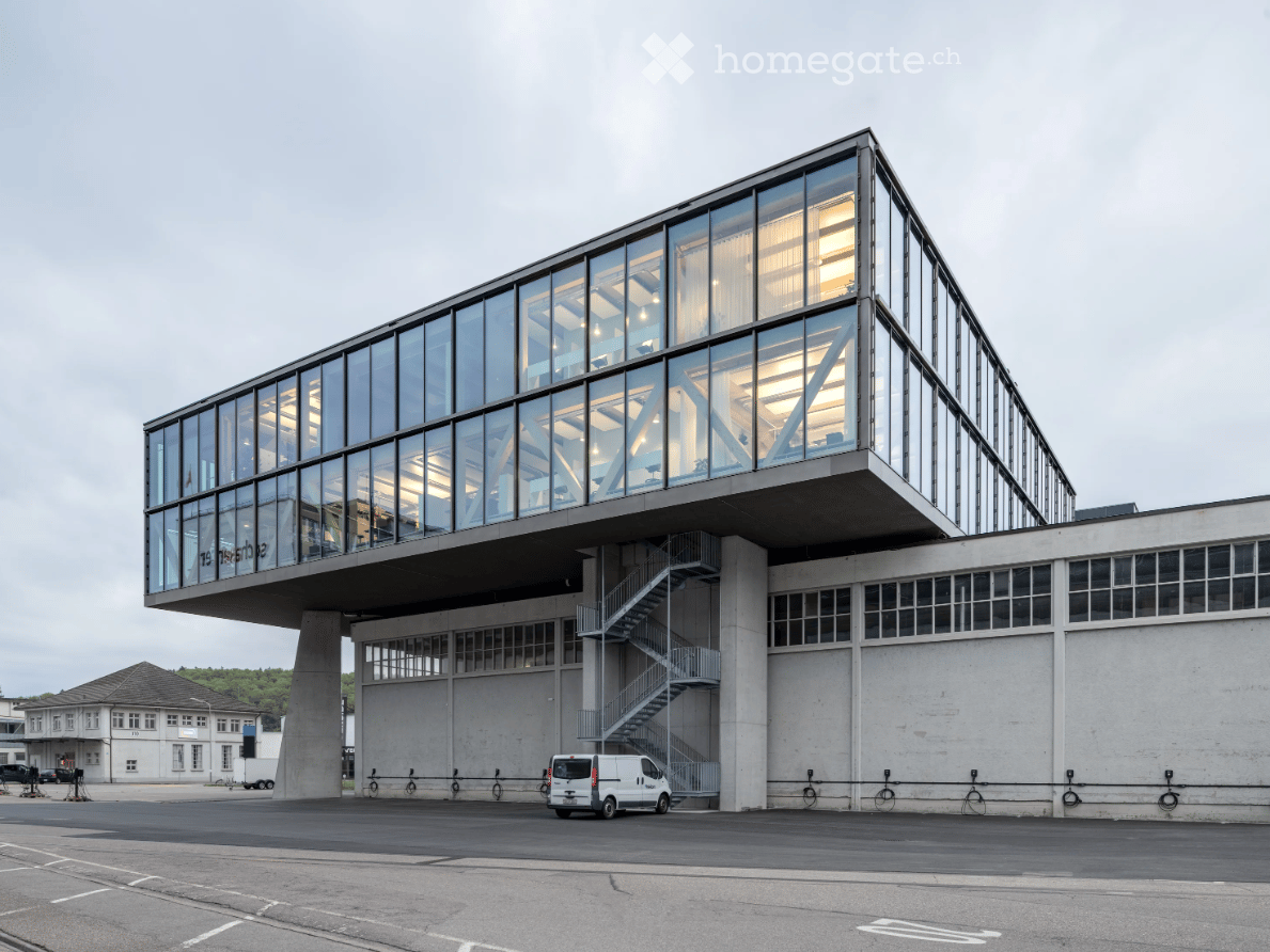 Modern building with glass facades, raised ground floor, stairs, parking lot, white van parked