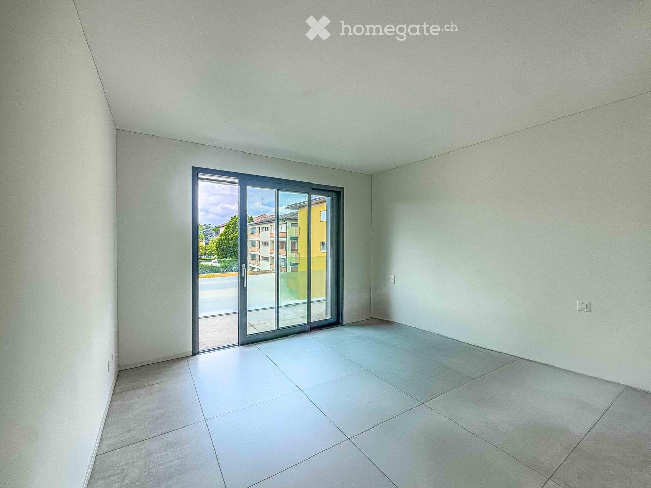 Empty room, white walls, gray floor, sliding glass door leading to a balcony