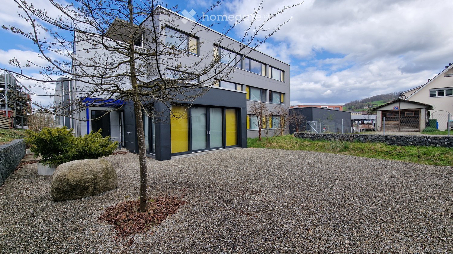 3 story house, yellow and grey walls, large windows, graveled driveway, plant