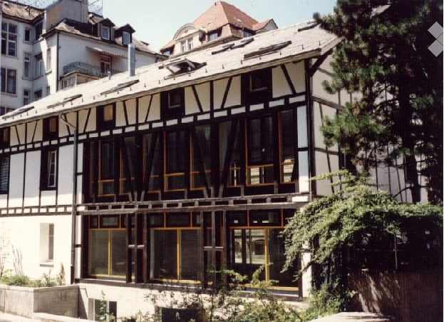white and black building, many windows, brown roof, wooden beams, plants in front