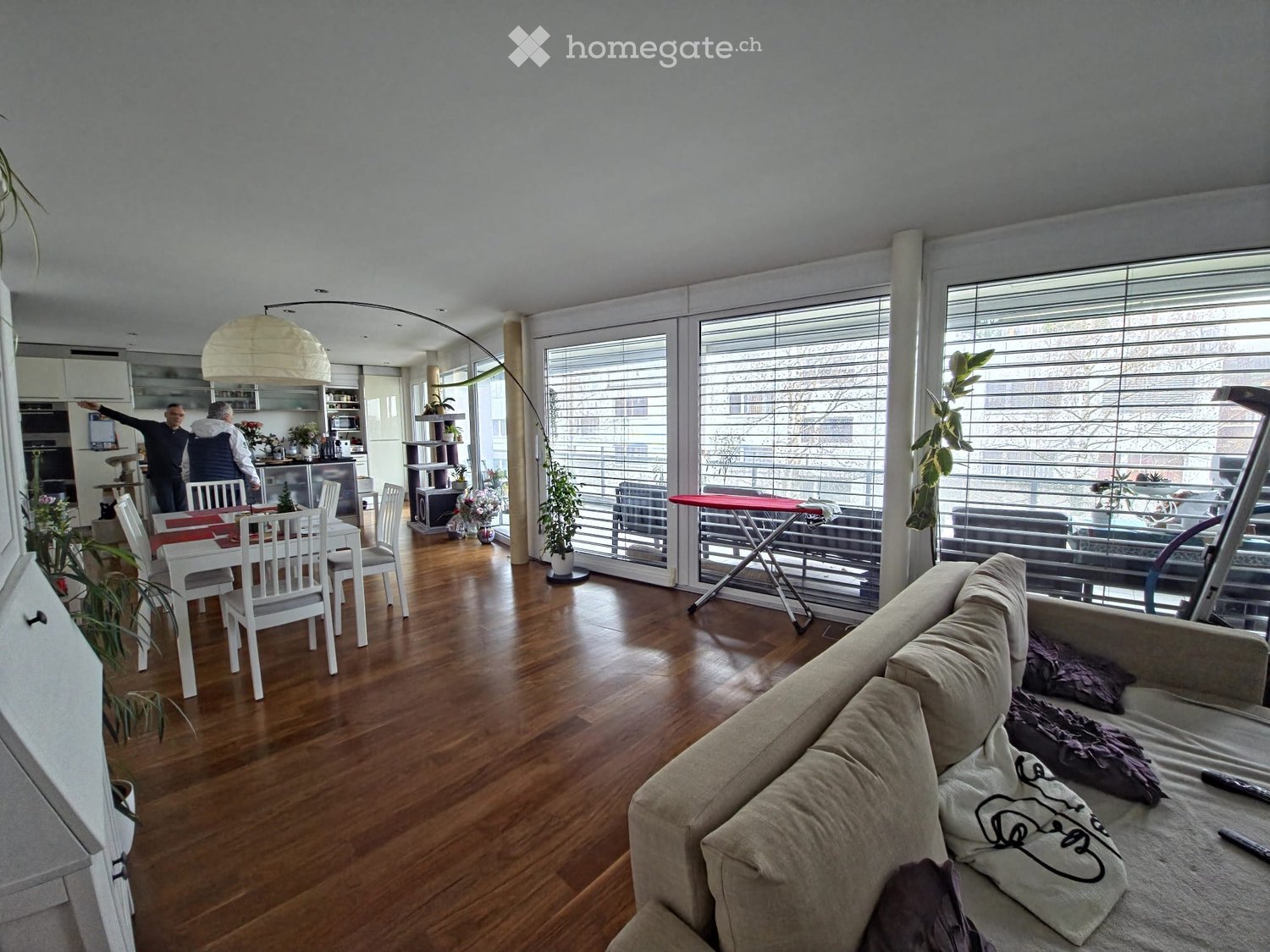 a spacious living room with hardwood floors, a dining table, a couch, large windows, and various indoor plants