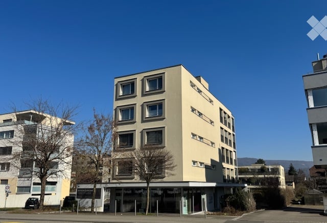Four-story beige building, multiple windows, raised ground floor