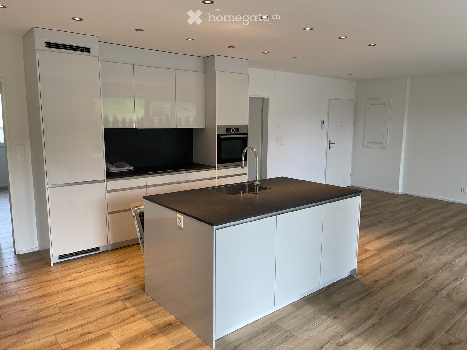 Modern kitchen with white cabinets, dark countertop, stainless steel appliances, and wooden flooring.