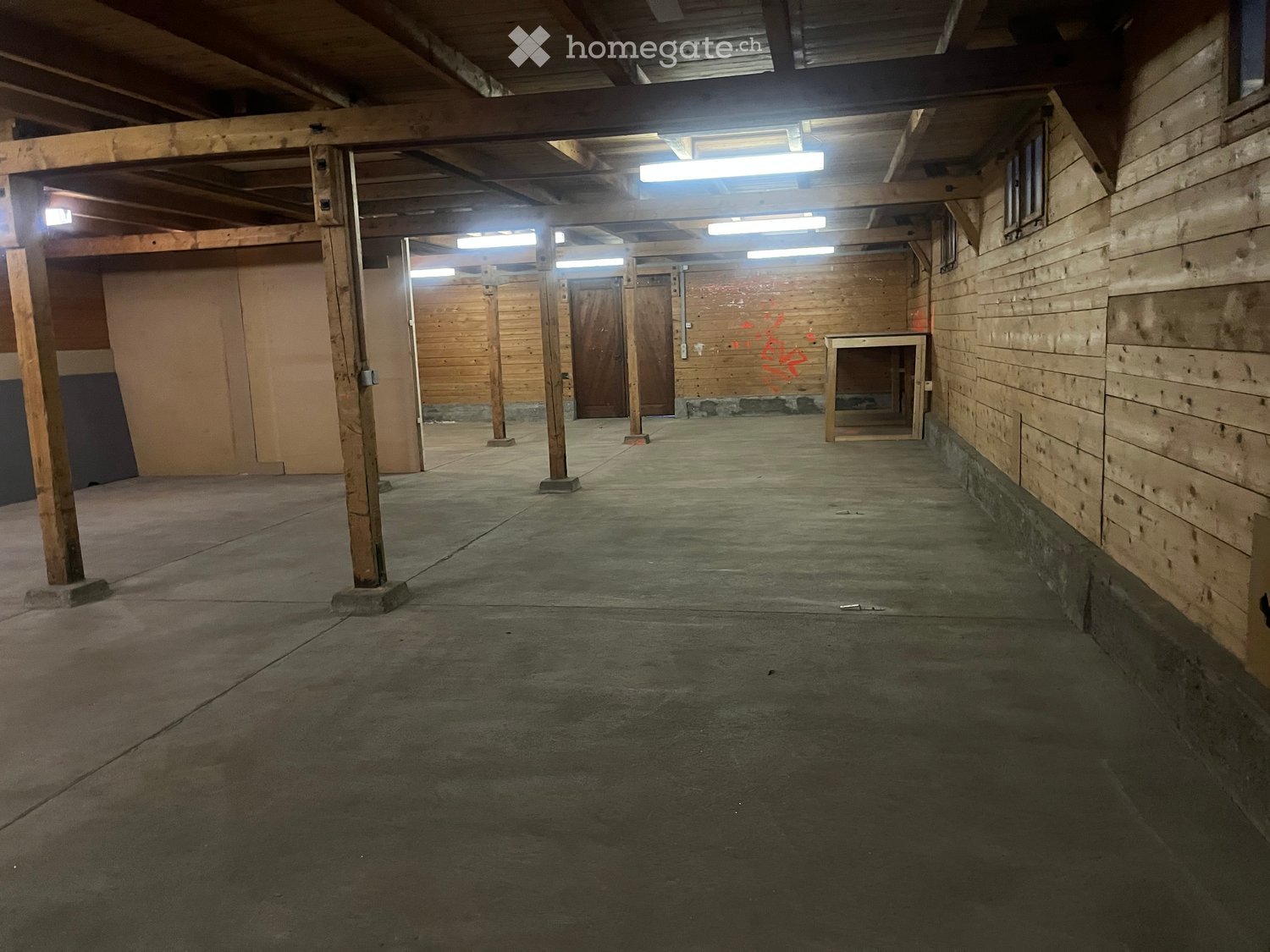 Empty room, wooden support columns, concrete floor, fluorescent lights, closed doors, wooden walls