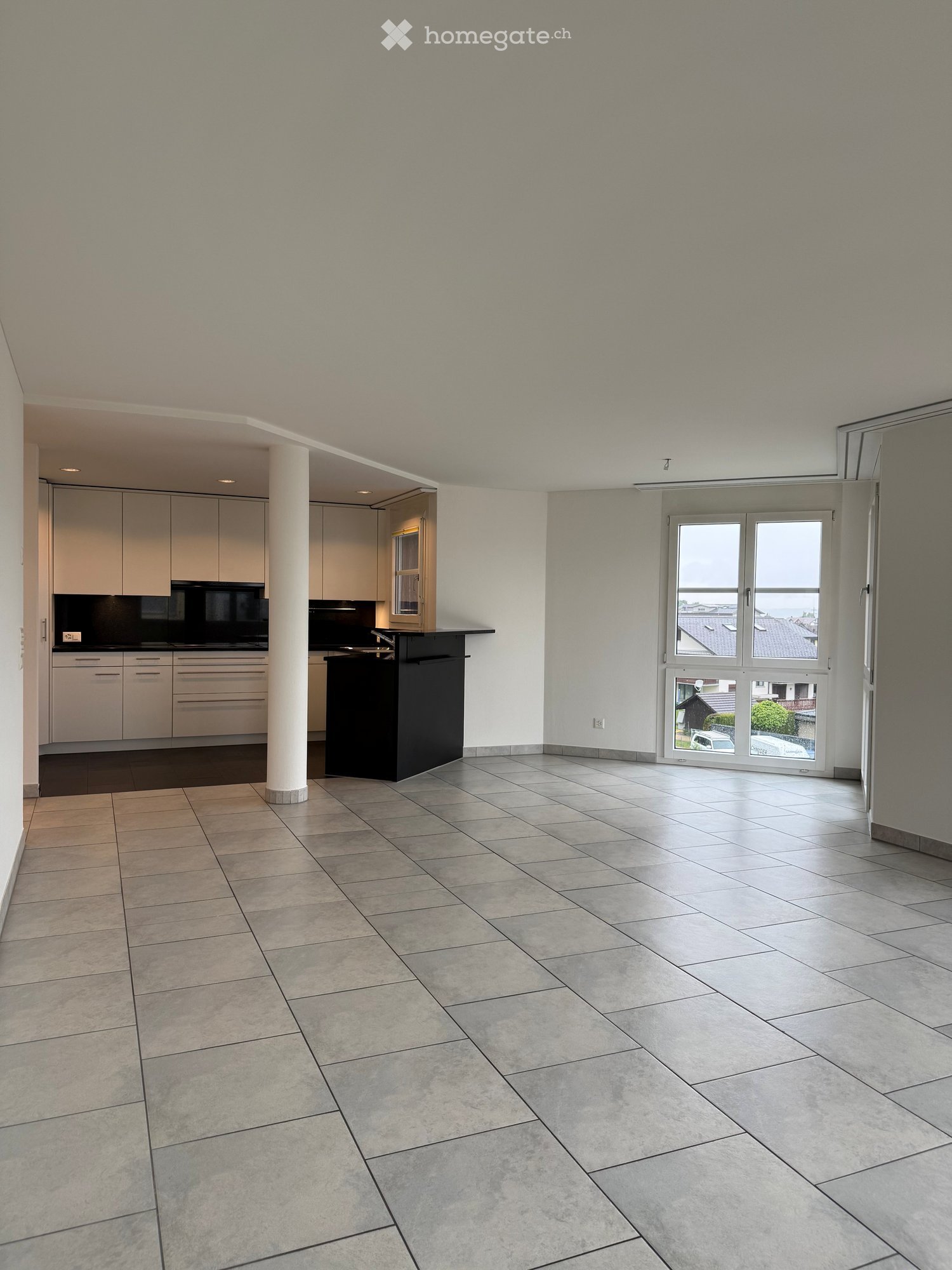 Unfurnished Room. Empty room with tiled floor, white walls, and large windows. Adjacent kitchen area with cabinets and appliances visible.