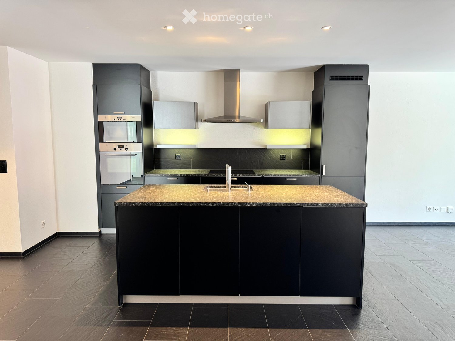 Modern kitchen with dark grey cabinets, stainless steel appliances, a central island with a granite countertop, and built-in lighting.
