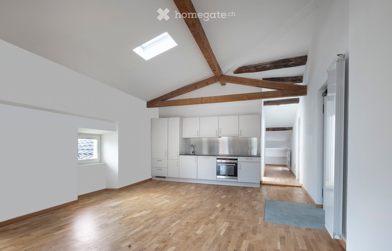 large open space, wooden floors, white kitchen, stainless steel appliances, large window, skylight
